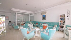 A lobby with teal sofas, white armchairs, a white coffee table, and a bookshelf. - Karbel Beach Hotel (Fethiye)