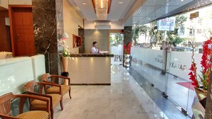 A hotel reception area with a marble reception desk, wooden chairs, and a glass barrier. - Galaxy Hotel (Mumbai)