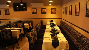 A restaurant with a long table set for dining, patterned seating, and framed pictures on the walls. - Galaxy Hotel (Mumbai)