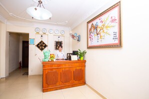 A reception area with a wooden desk, a clock, a framed artwork, and a potted plant.