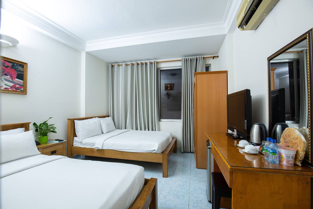 A hotel room with two beds, a desk with a mirror, a television, and a window with curtains.