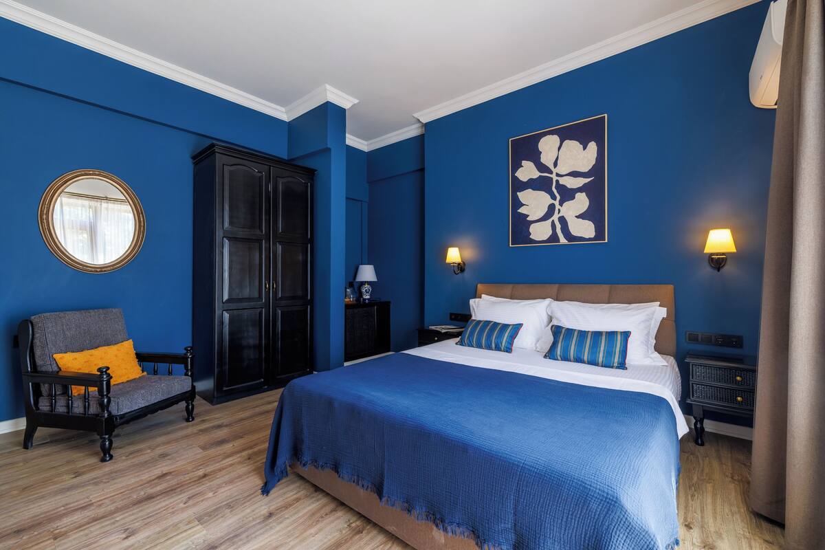 A bedroom with a large bed, a dark wooden wardrobe, a round mirror, and two wall-mounted lamps.