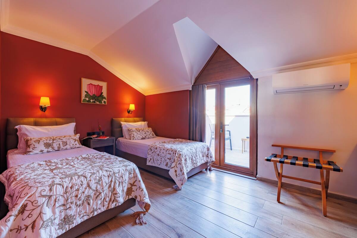 A bedroom with two beds, a bench, and a window.