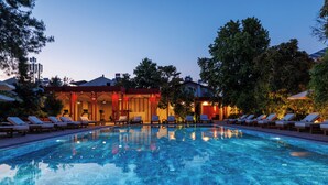 Ein Schwimmbecken mit Liegestühlen, ein Gebäude mit roter Fassade und Bäume im Hintergrund.