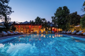 Une piscine avec des chaises longues, un bâtiment à la façade rouge et des arbres en arrière-plan.