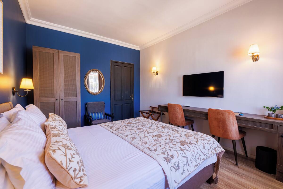 A hotel room with a bed, desk, chairs, a TV, and a wardrobe.