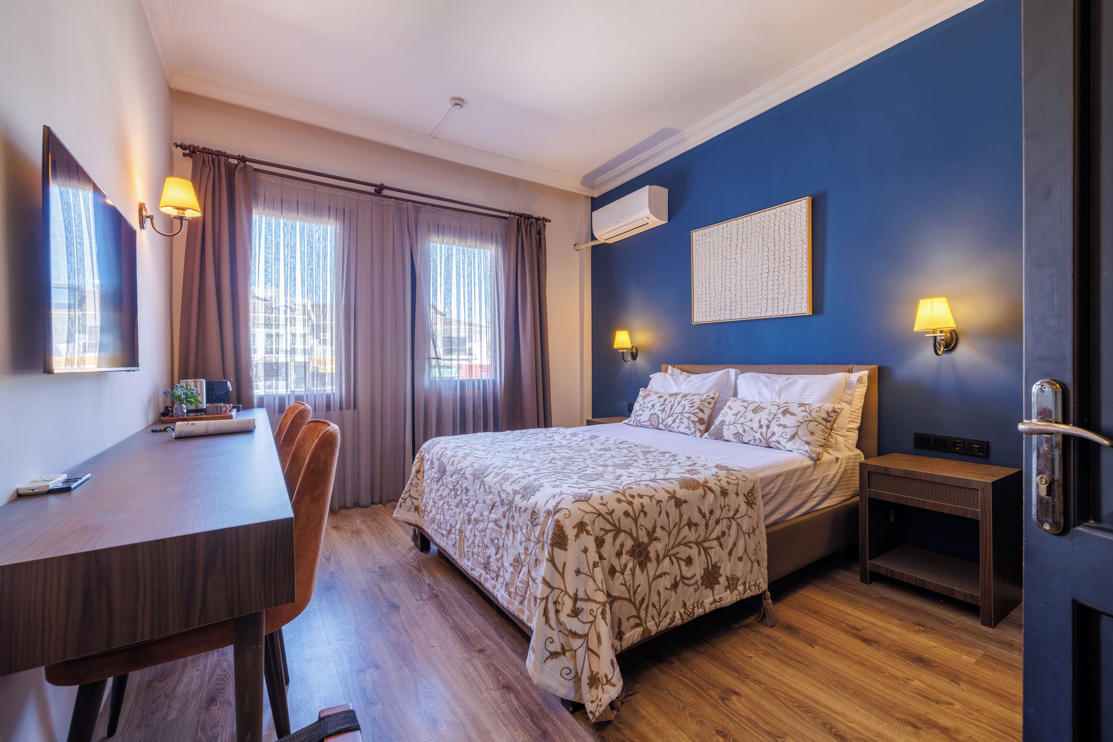 Une chambre d’hôtel équipée d’un lit, d’un bureau, d’une chaise, d’un climatiseur et d’une œuvre d’art accrochée au mur.