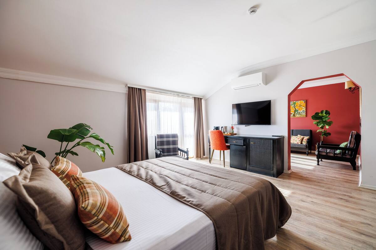 A hotel room with a bed, a desk, a TV, and a red accent wall.