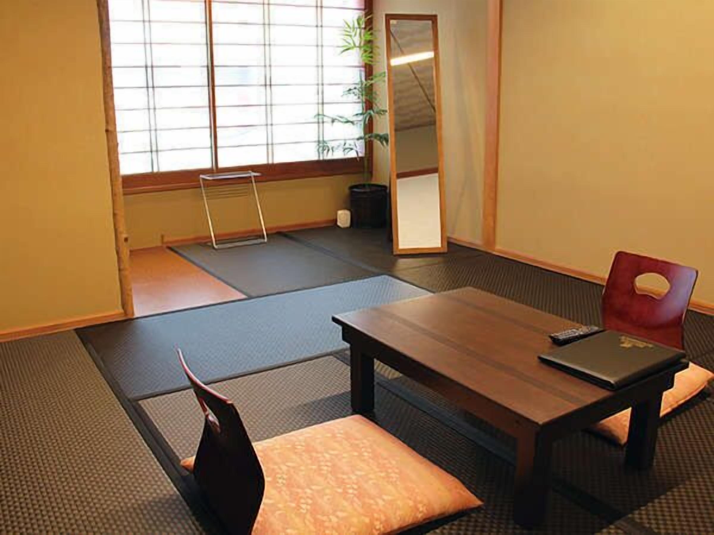 A tatami mat room with a wooden table, a red chair, and a black laptop.