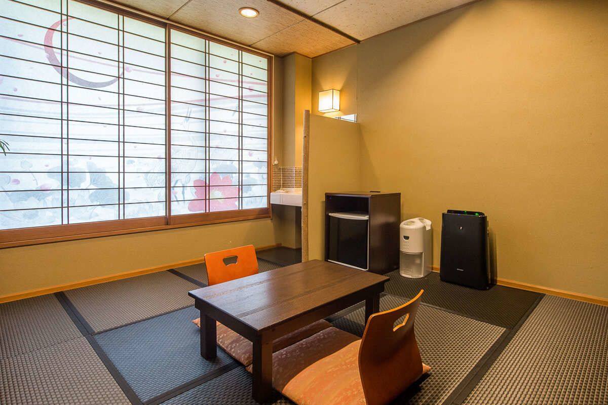 A tatami mat room with a low table and chairs, a heater, a refrigerator, and a speaker.