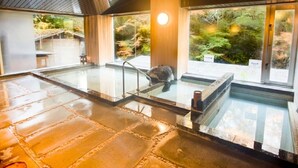 A modern indoor pool area with a stone floor, glass walls, and a view of a forested landscape. - LiVEMAX RESORT Amagi-Yugashima (Izu)