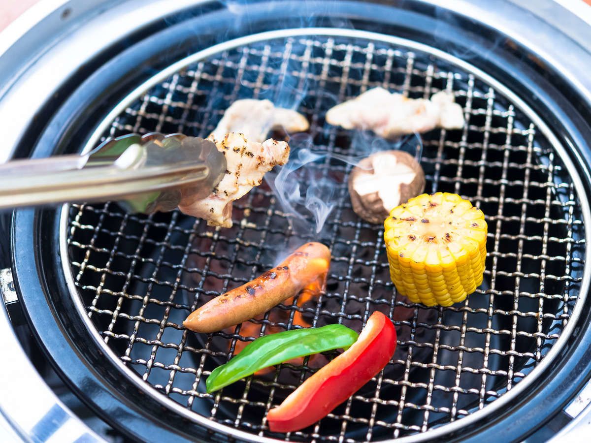 Un barbecue où divers aliments sont en train de cuire, notamment des saucisses, des crevettes, du maïs et des légumes.