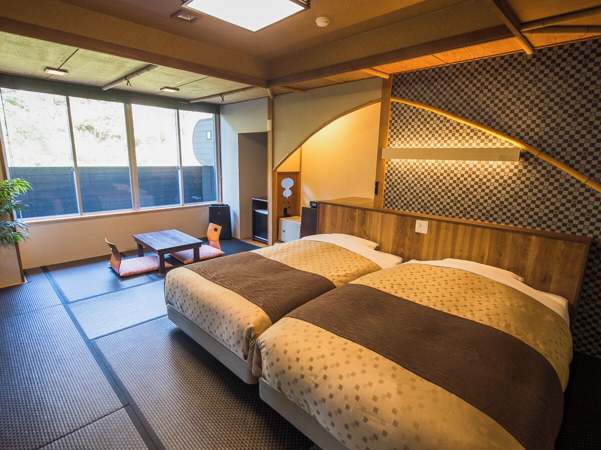 A hotel room with a large bed, a small table, and a view of the outdoors through the window.