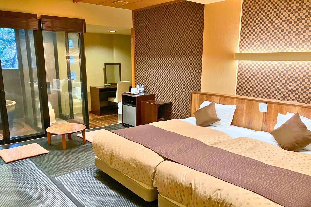 A hotel room with a large bed, a desk, a chair, and a view through a glass door.
