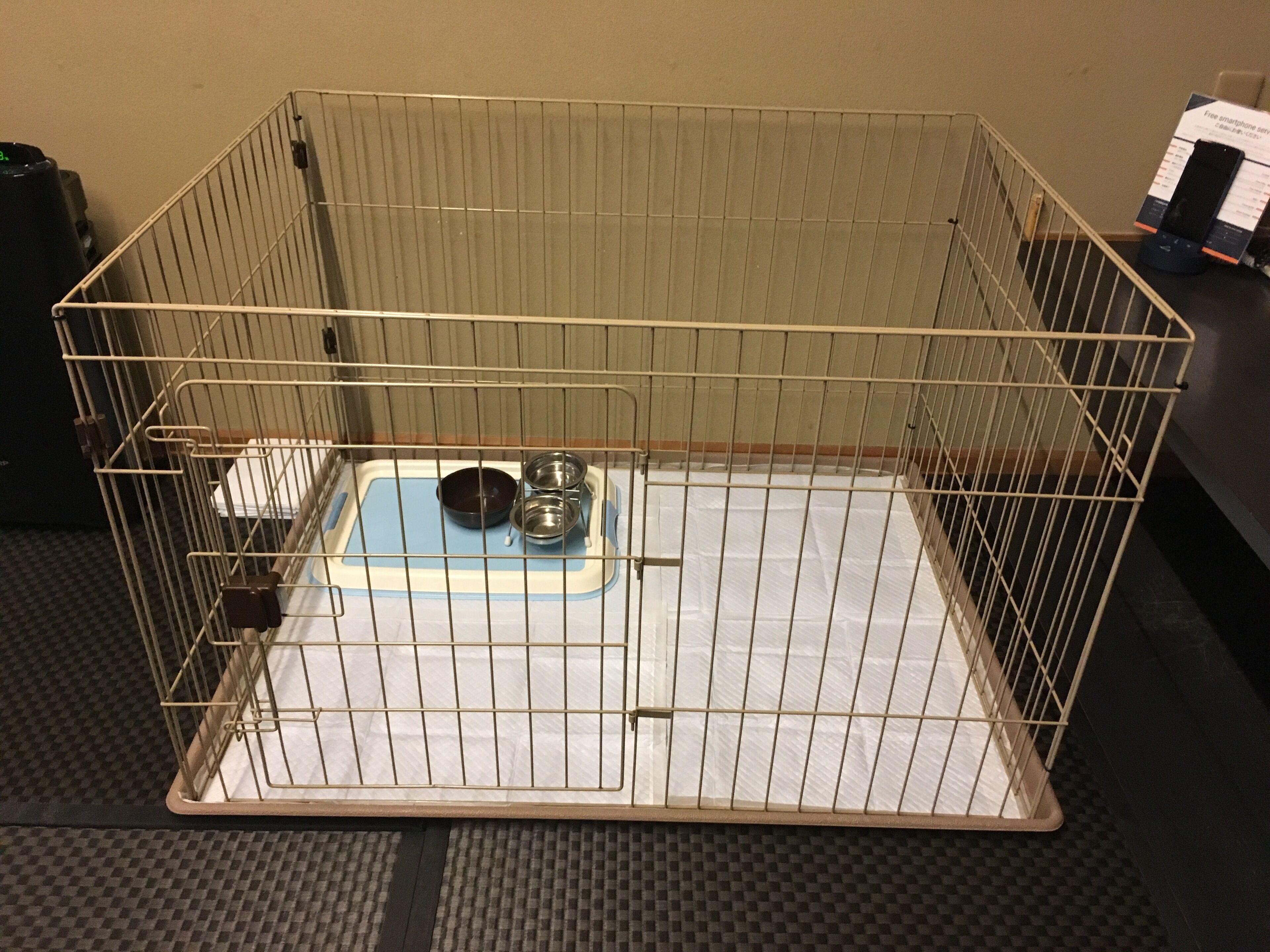 A metal cage with a blue water bowl and a metal food bowl.