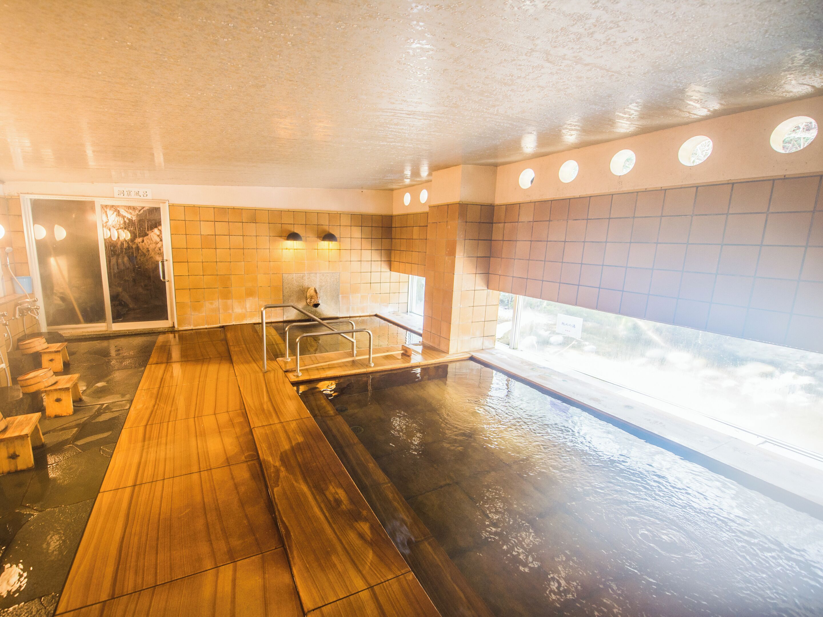 A hot tub area with a wooden deck, a glass door entrance, and tiled walls.