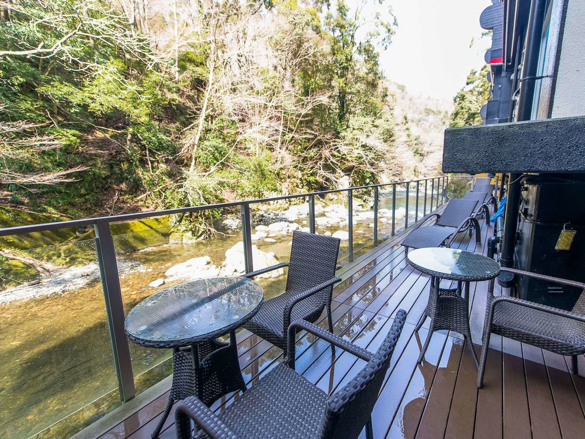 A deck with outdoor seating overlooking a river, surrounded by trees.