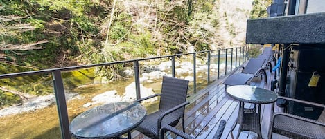 A deck with outdoor seating overlooking a river, surrounded by trees.