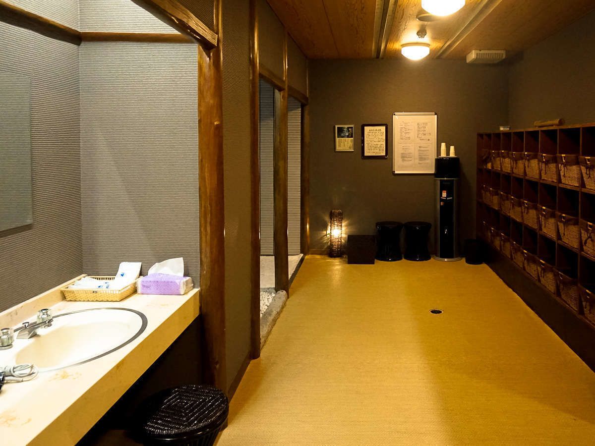 A restroom with a wooden floor, a sink with a mirror, and a wall-mounted trash bin.
