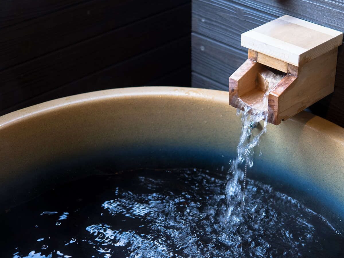 A wooden water spout pouring water into a large, dark-colored basin.