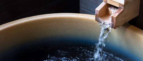 A wooden water spout pouring water into a large, dark-colored basin.