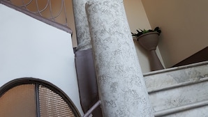 Una escalera con barandilla metálica, un pilar texturizado y un aplique de pared.