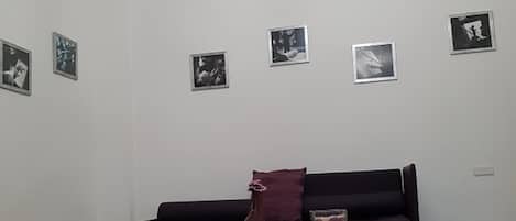 A living room with a dark sofa, a glass coffee table, and a purple rug. There are four framed pictures on the wall.