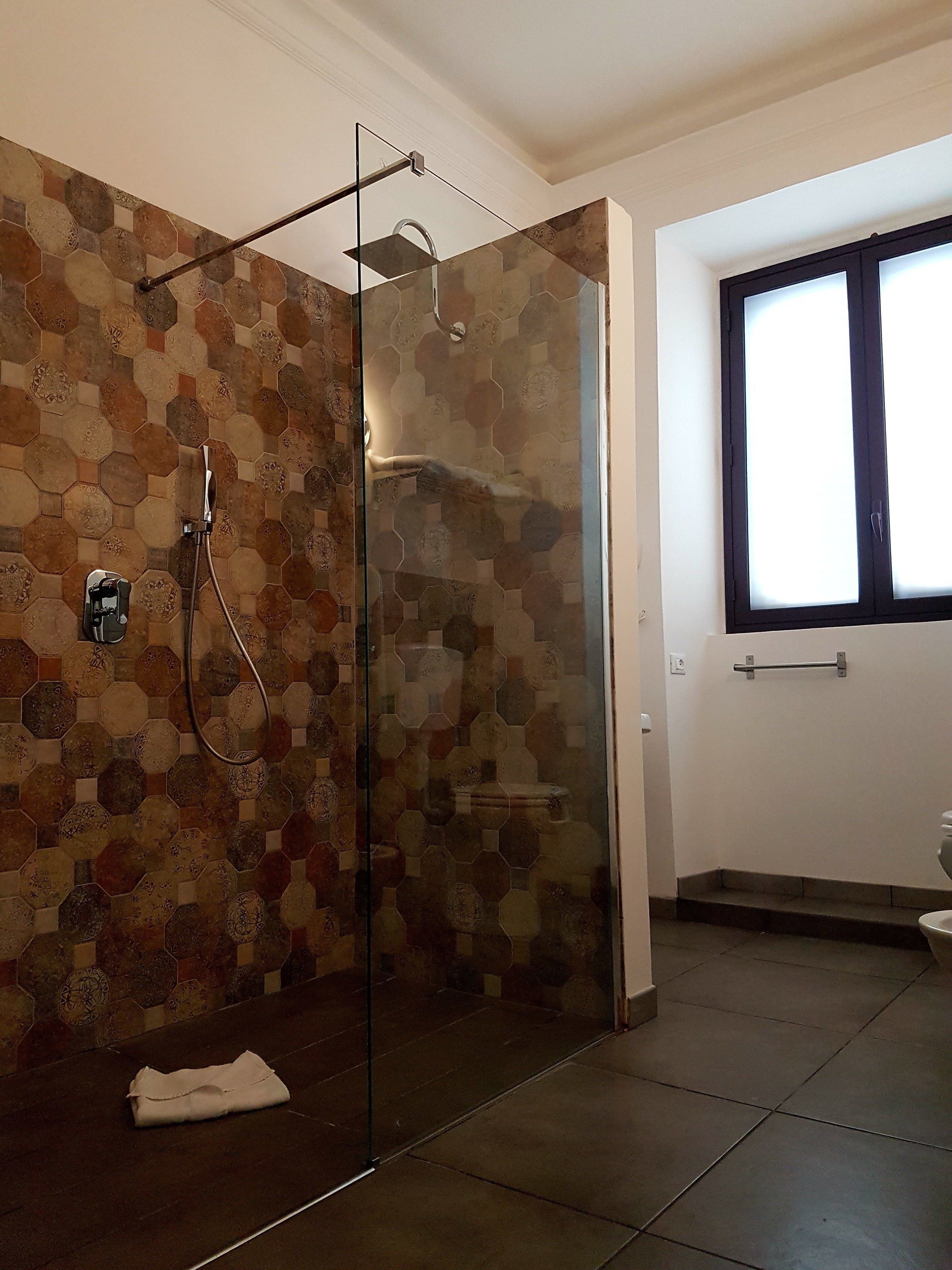 Un bagno moderno con box doccia in vetro, pavimento piastrellato e finestra che lascia entrare luce naturale.