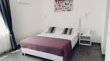 A modern bedroom with a white bed, two pillows, a red blanket, a nightstand with a remote, and a wall art piece.