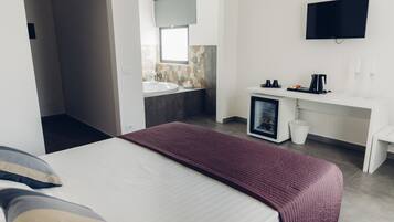 Een moderne hotelkamer met een bed, een badkamer met een wastafel, een televisie en een klein bureau met een koffiezetapparaat.