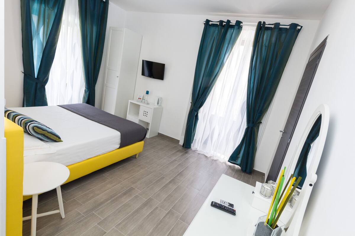 Una camera d'albergo moderna con un letto, una scrivania, una sedia, una TV e tende.