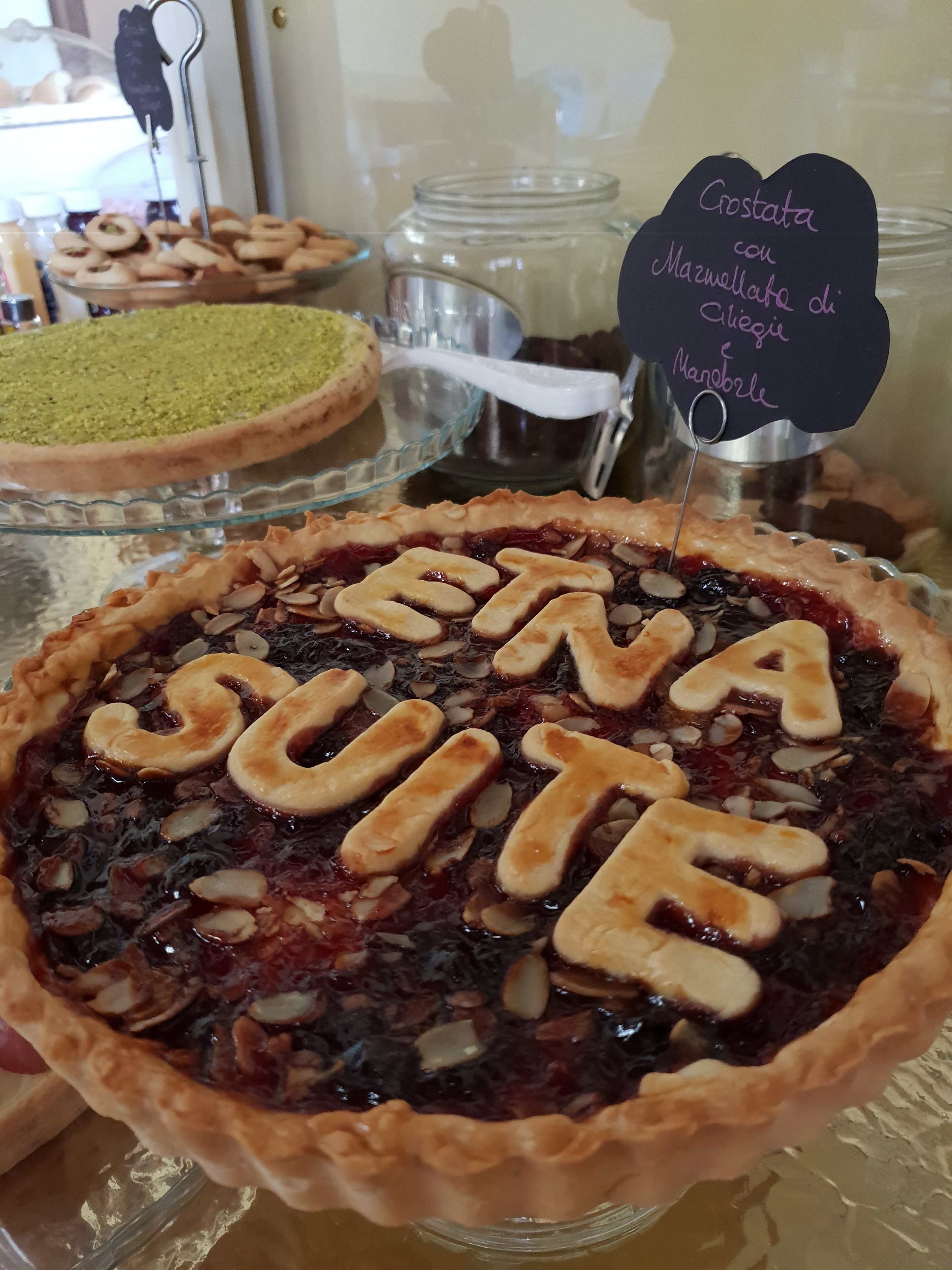 A dessert display with a tart labeled "Crostata con Mazzarella di Sbaglia e Mandorle" and another with "ETNA SUITE" written on it.