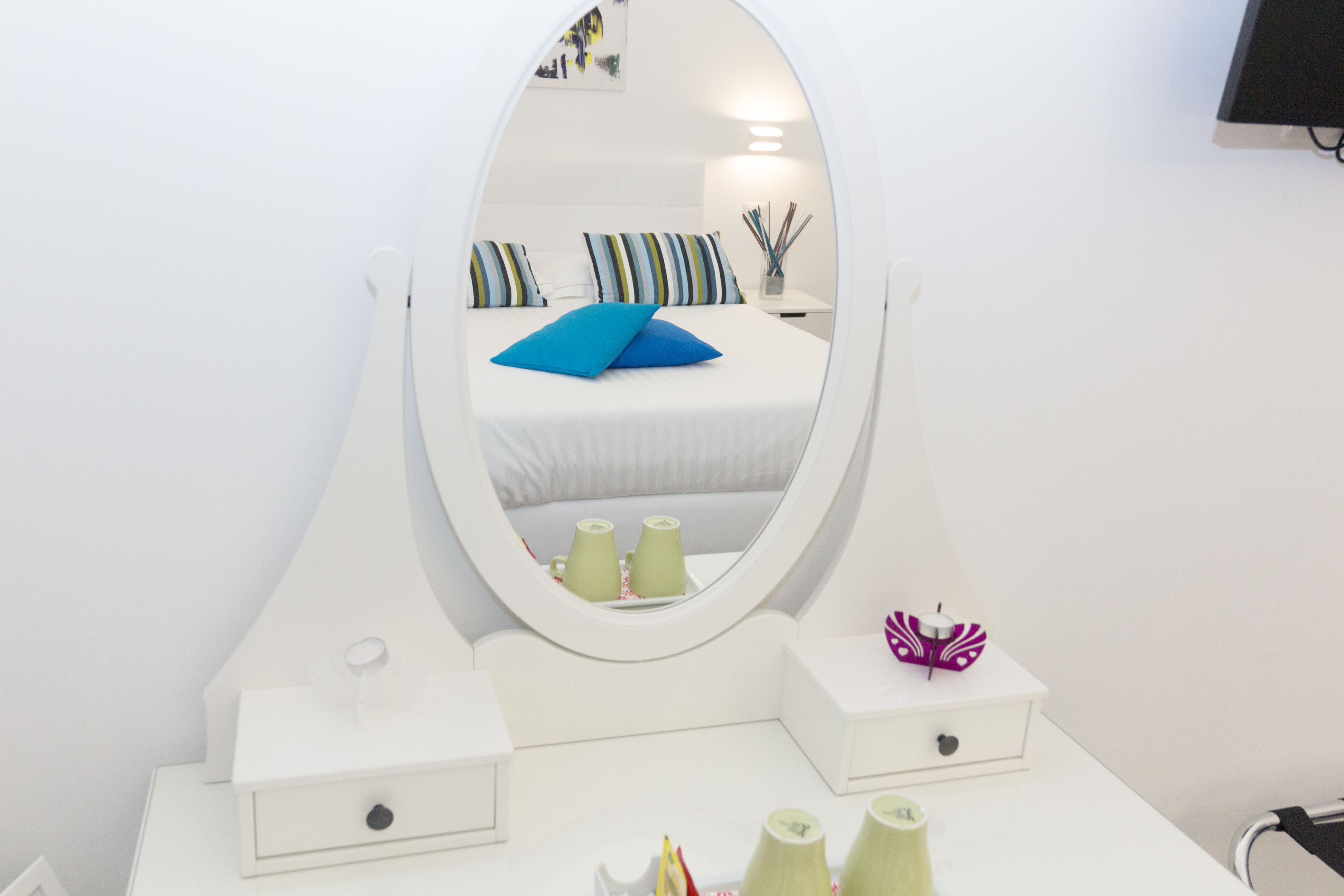 A white vanity with a mirror, a bed with striped pillows, and a small table with a purple butterfly ornament.