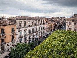 Una hilera de edificios históricos con balcones, una calle arbolada y cielo despejado.