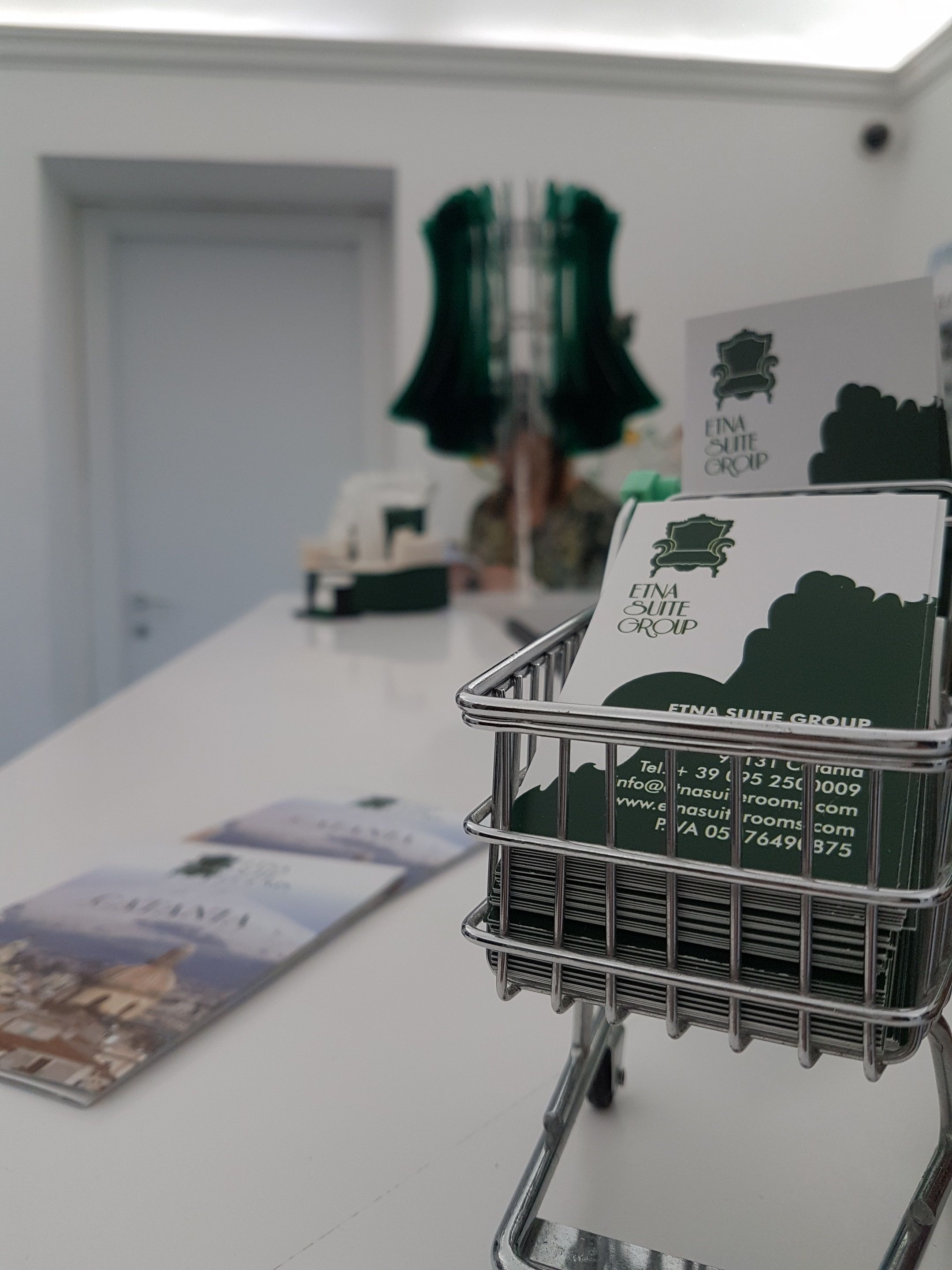 A metal cart with a green brochure for ETNA SUITE GROUP, a white door, and a green chair in the background.
