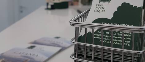 A metal cart with a green brochure for ETNA SUITE GROUP, a white door, and a green chair in the background.