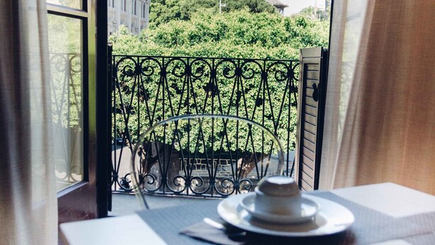 Un balcón con una mesa dispuesta para dos personas, con vista a un parque verde y un edificio.