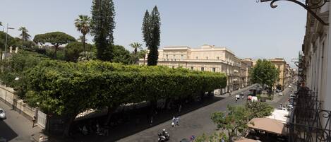 A street view with a building featuring a covered outdoor seating area and a large tree.
