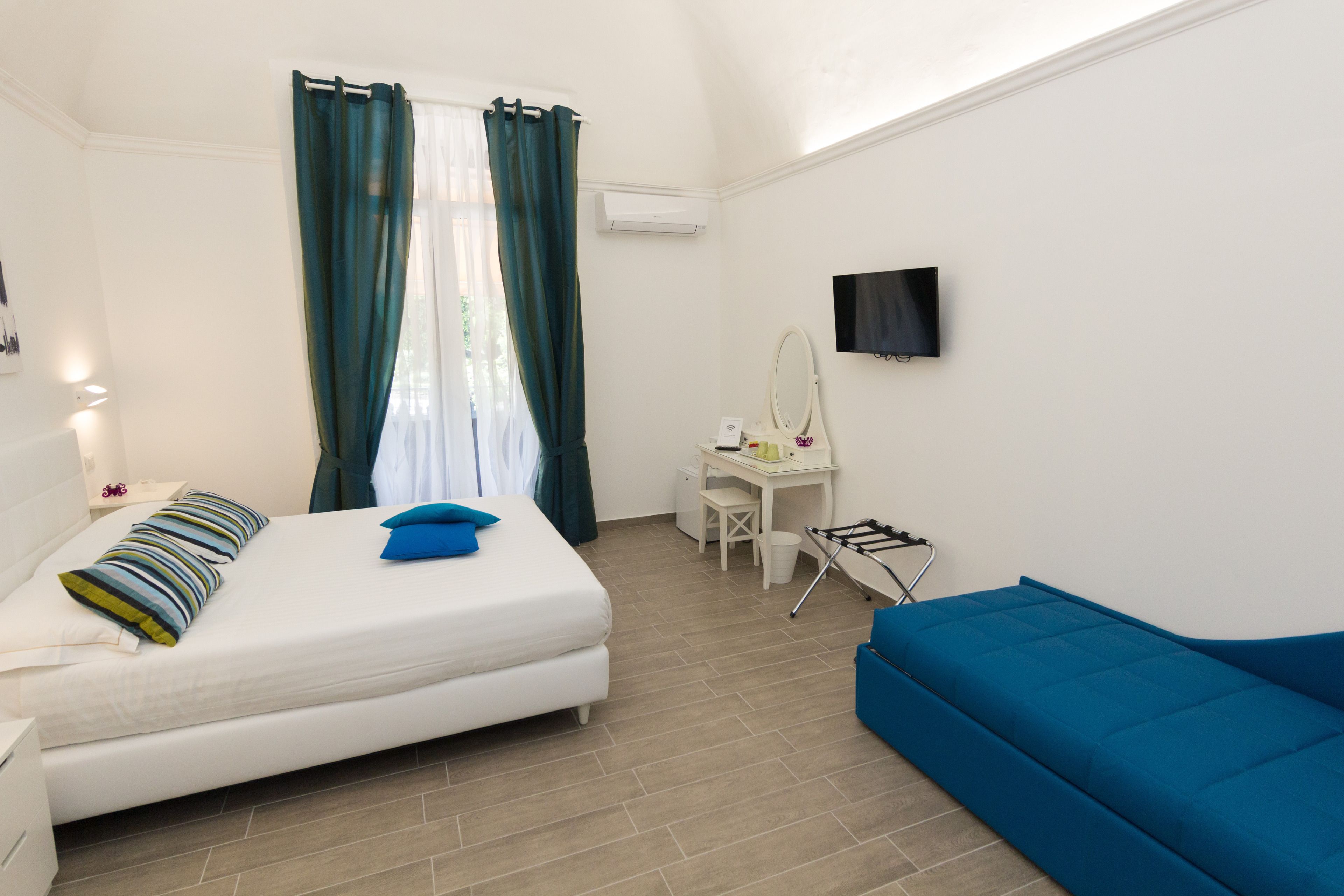 Un dormitorio con cama, escritorio, silla, sofá azul y televisión.