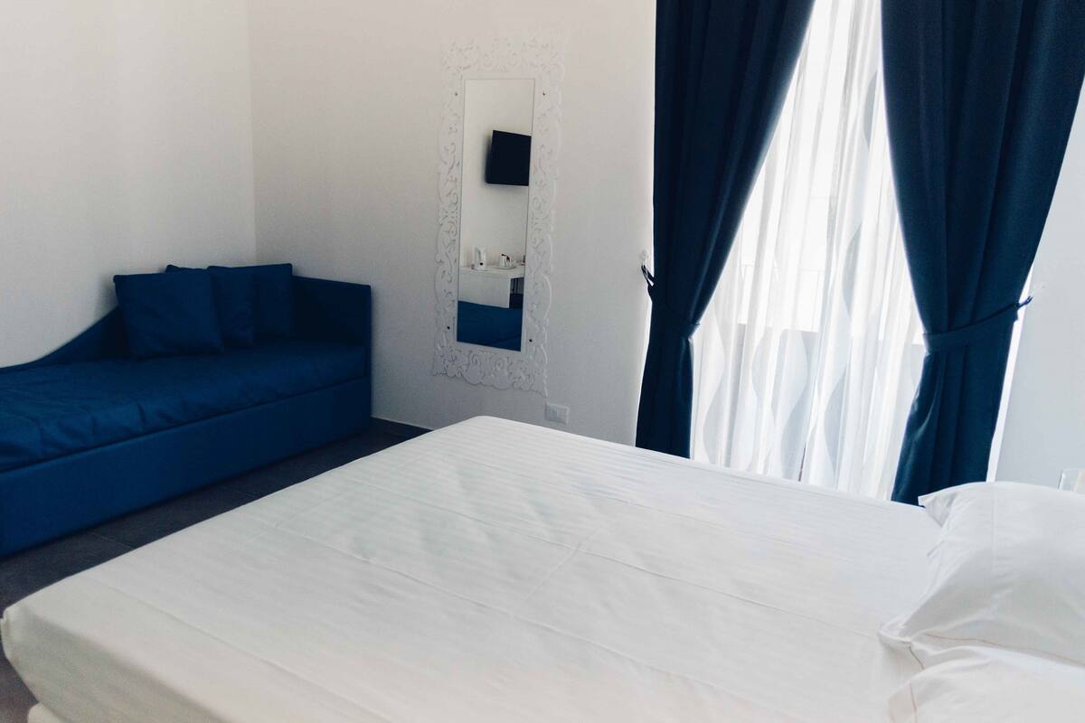 Una camera d'albergo con un letto, un divano blu, una parete bianca e uno specchio.