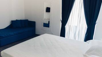 A hotel room with a bed, a blue sofa, a white wall, and a mirror.
