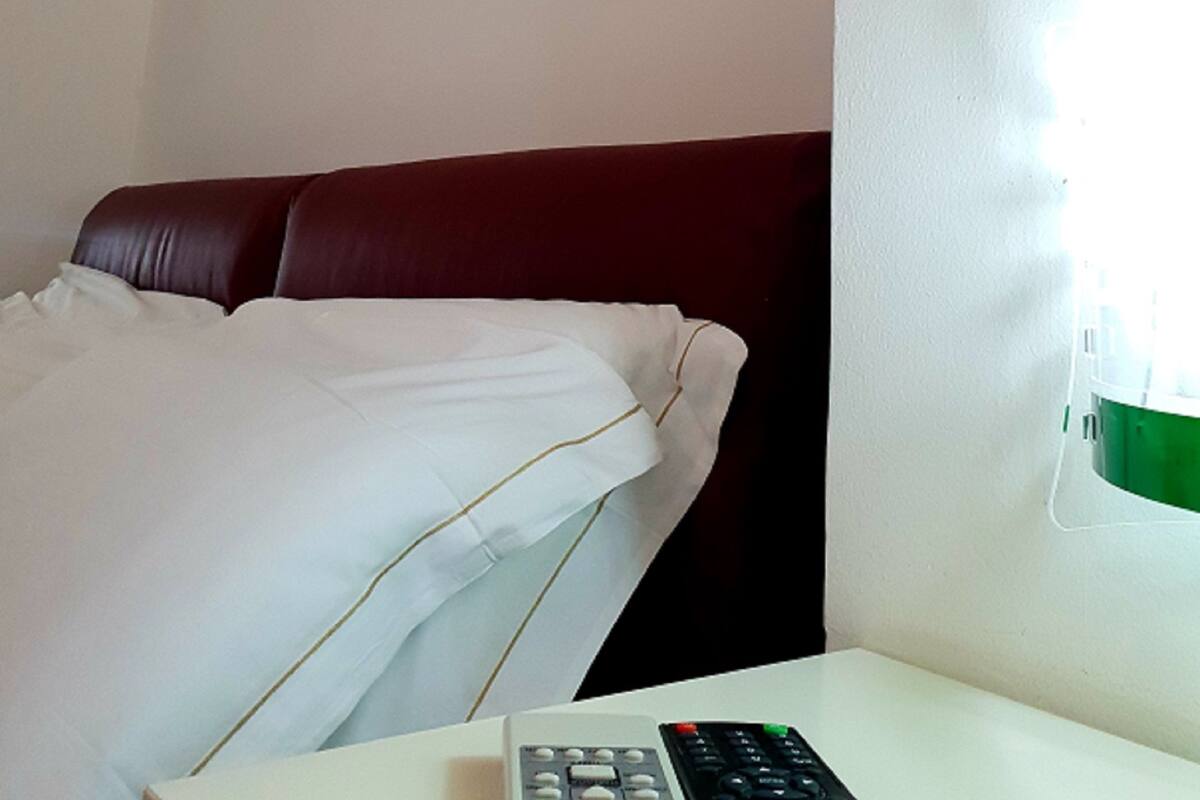 Una camera d'albergo con un letto, un comodino, un telecomando e un'opera d'arte appesa al muro.