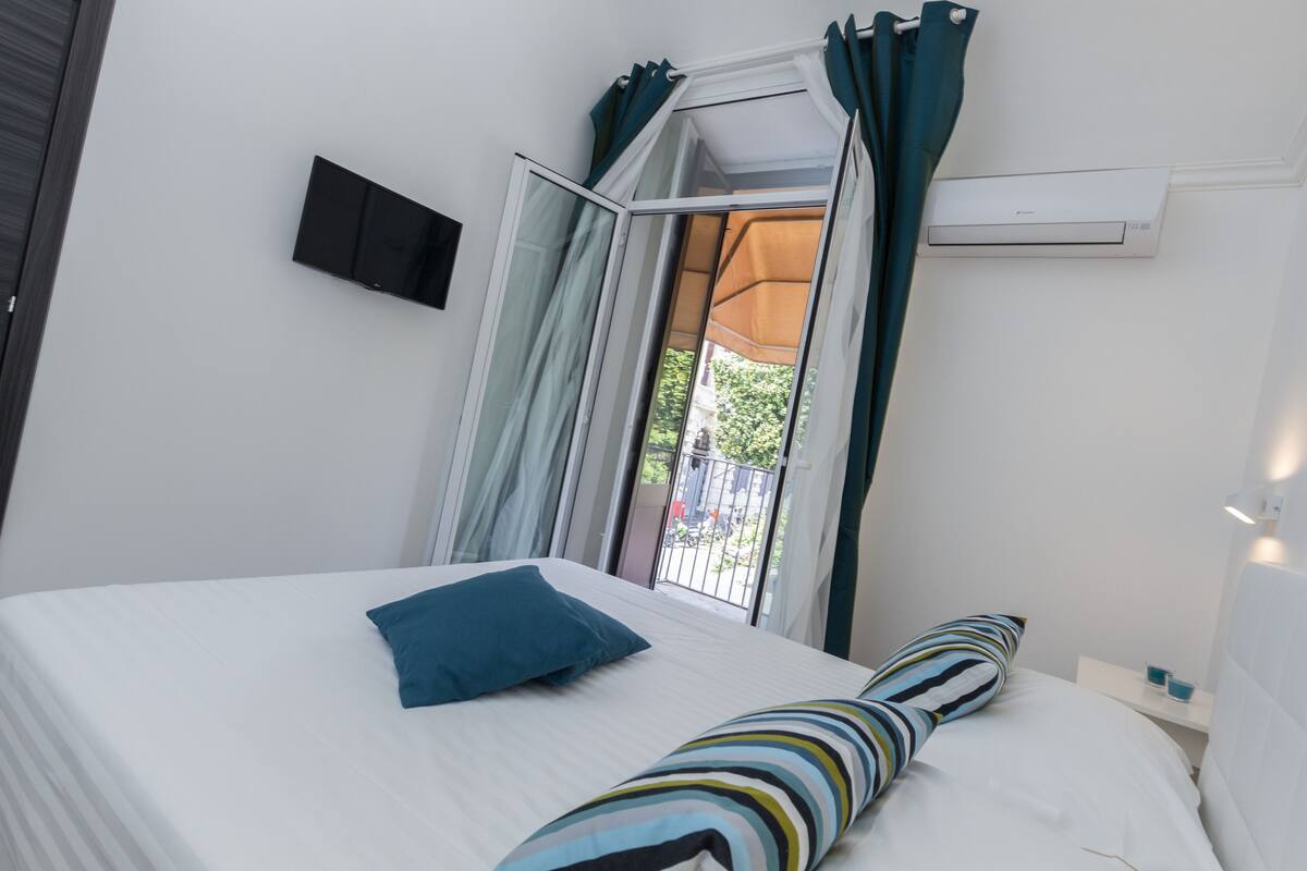 Una camera da letto con un letto, una TV, una finestra con tende e un condizionatore d'aria.