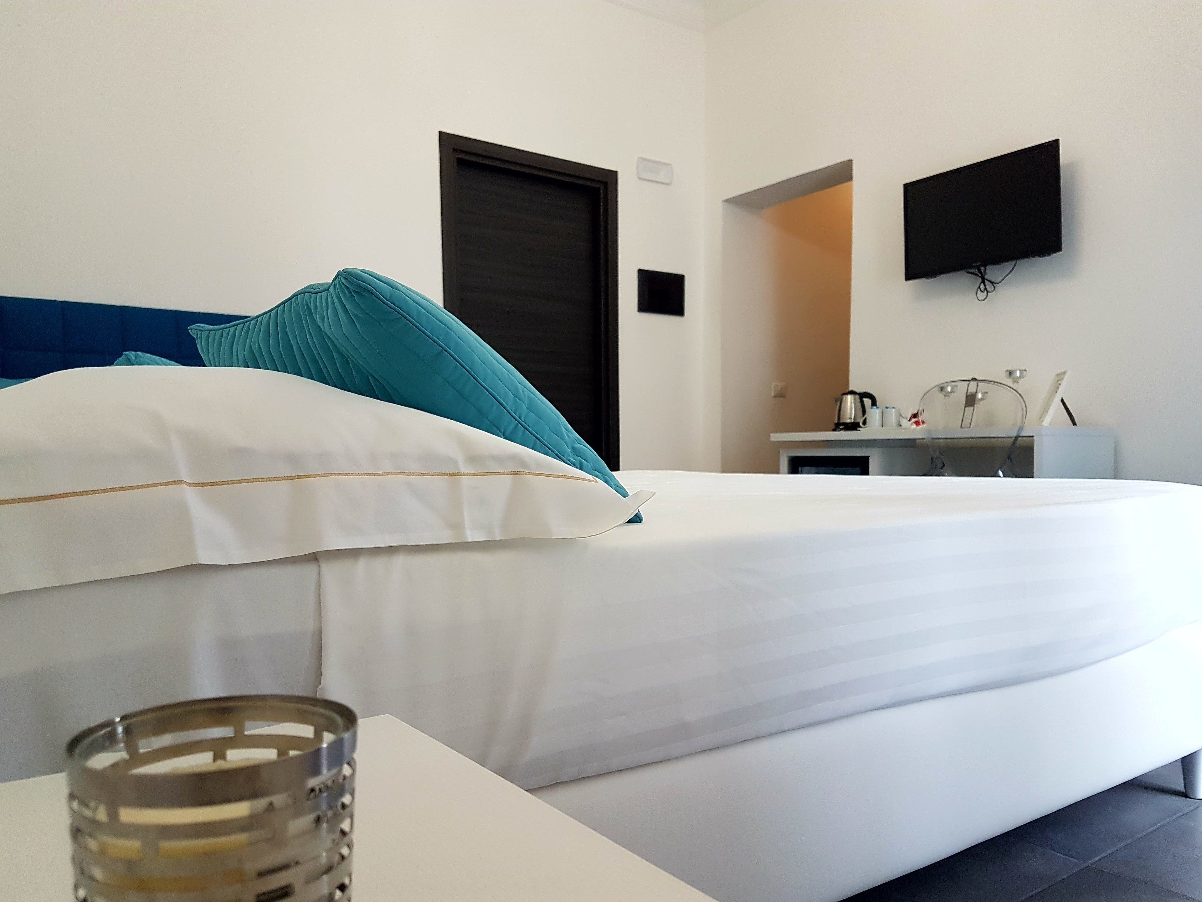 A hotel room with a bed, a bedside table, a TV mounted on the wall, and a kitchenette area.