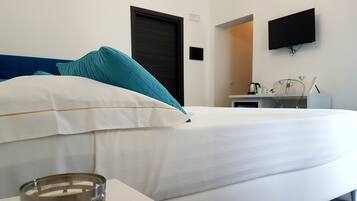 A hotel room with a bed, a bedside table, a TV mounted on the wall, and a kitchenette area.