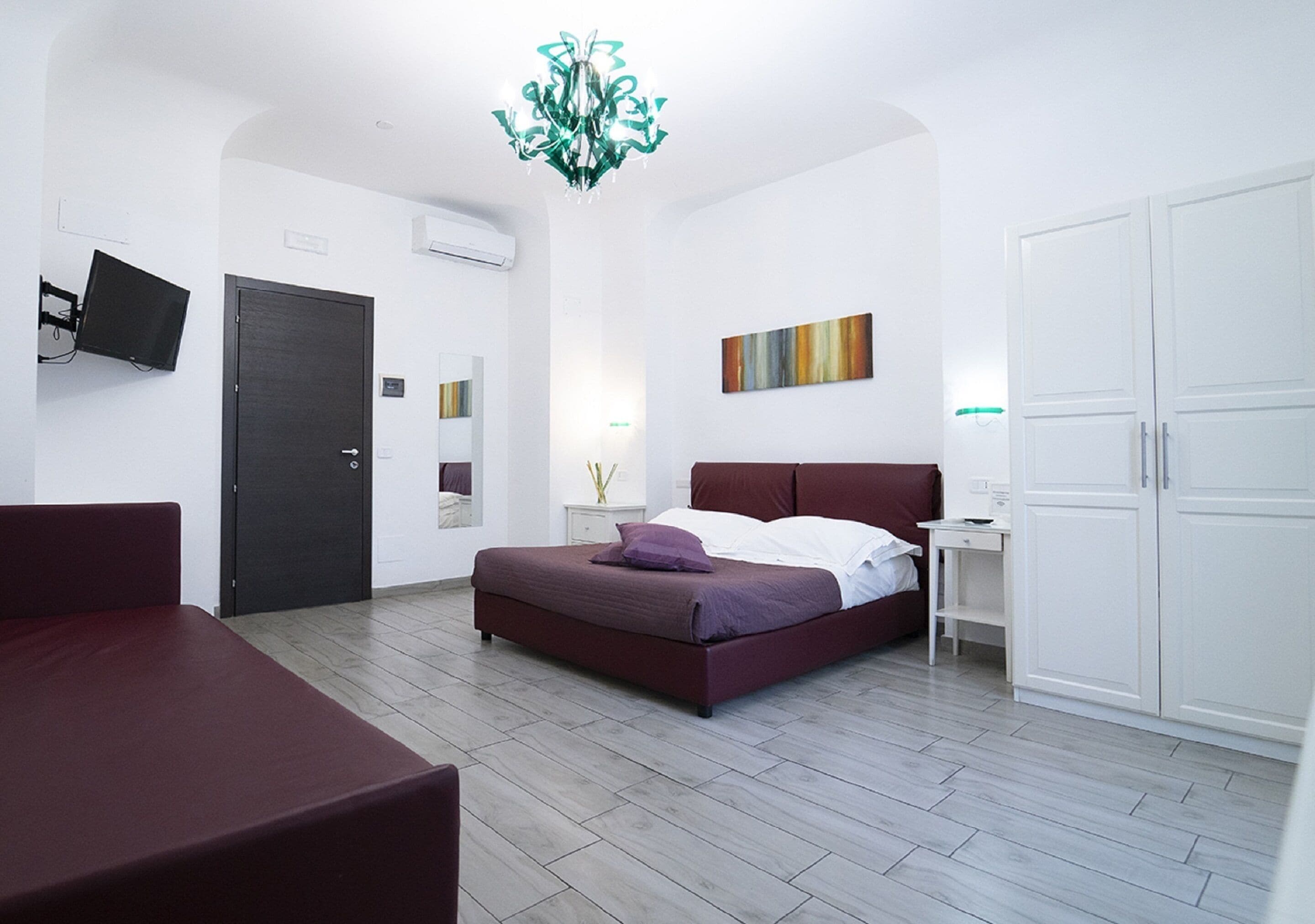 A modern bedroom with a bed, a TV, a wardrobe, and a chandelier.