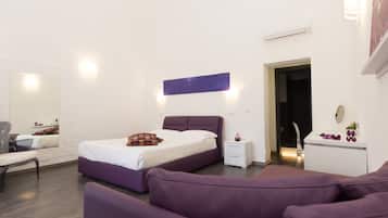 Un dormitorio moderno con una cama morada, paredes blancas y una mesita de noche pequeña y blanca.