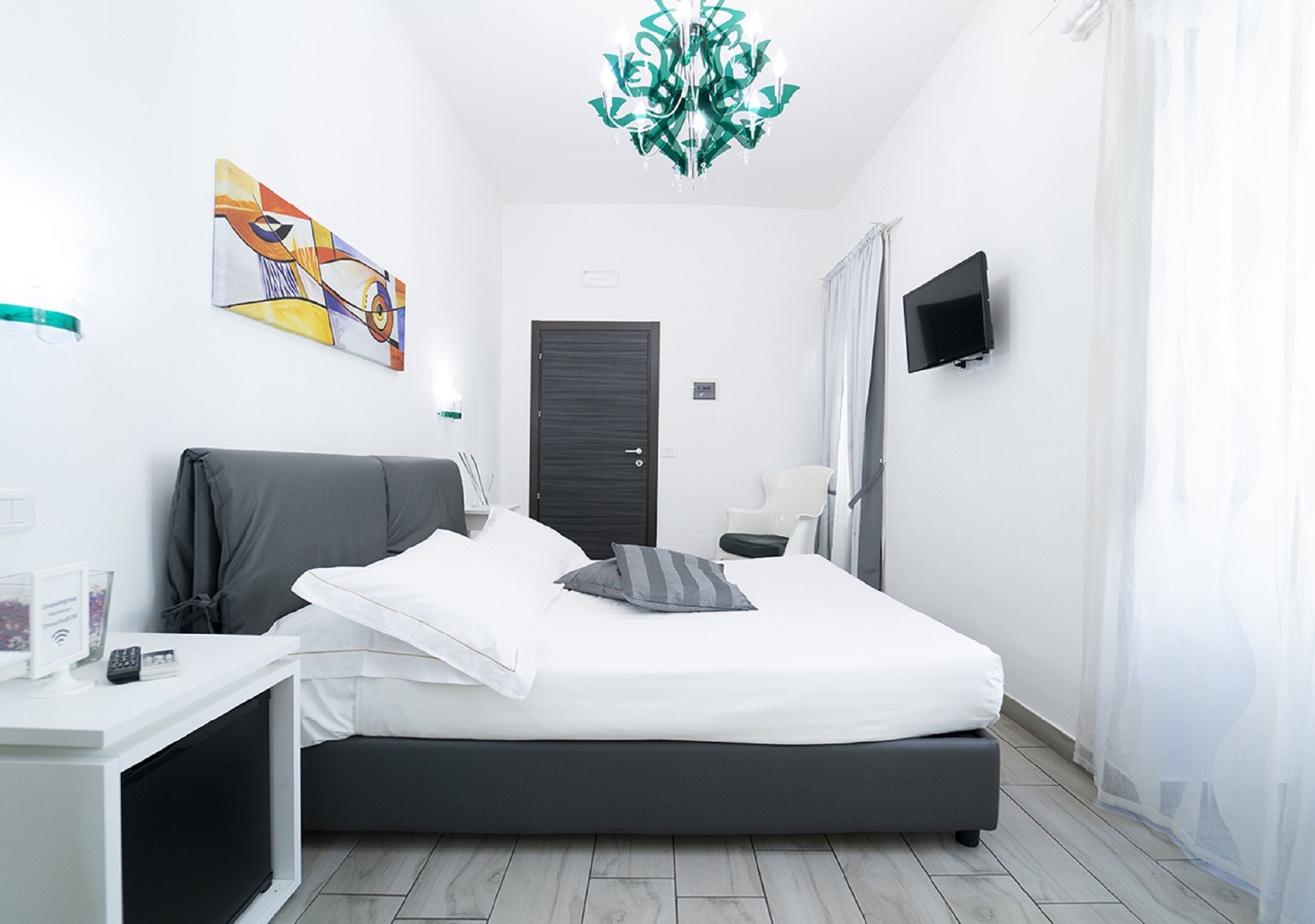 A modern bedroom with a bed, bedside table, TV, artwork, and a door.