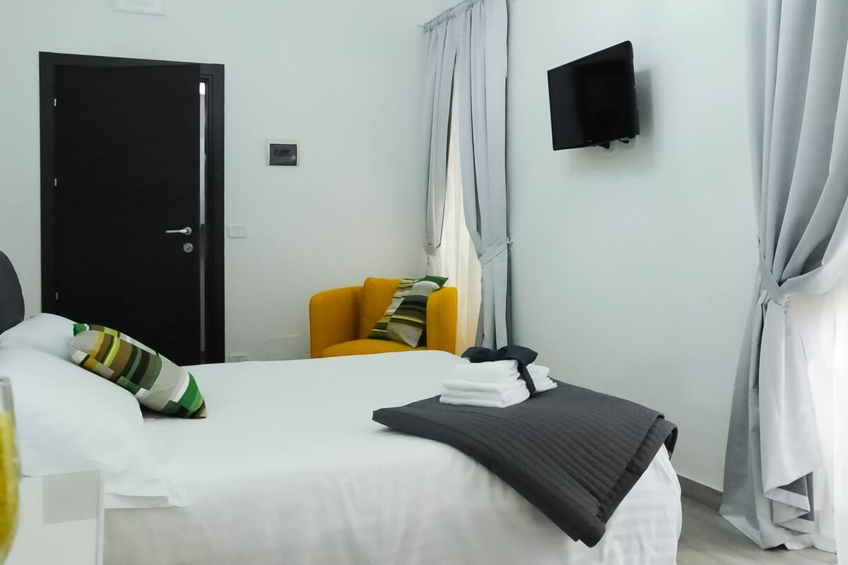 Una camera d'albergo con un letto, una sedia, una TV e tende.