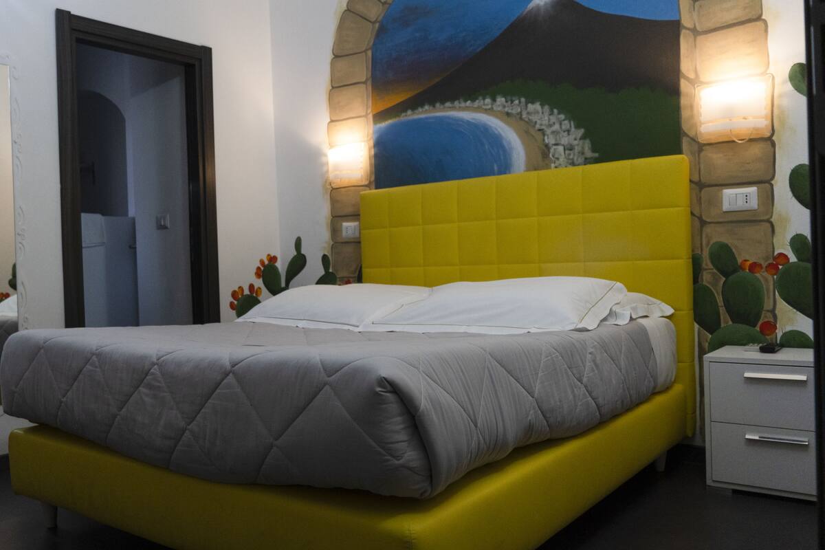 Un letto con copripiumino trapuntato grigio e testiera imbottita gialla.